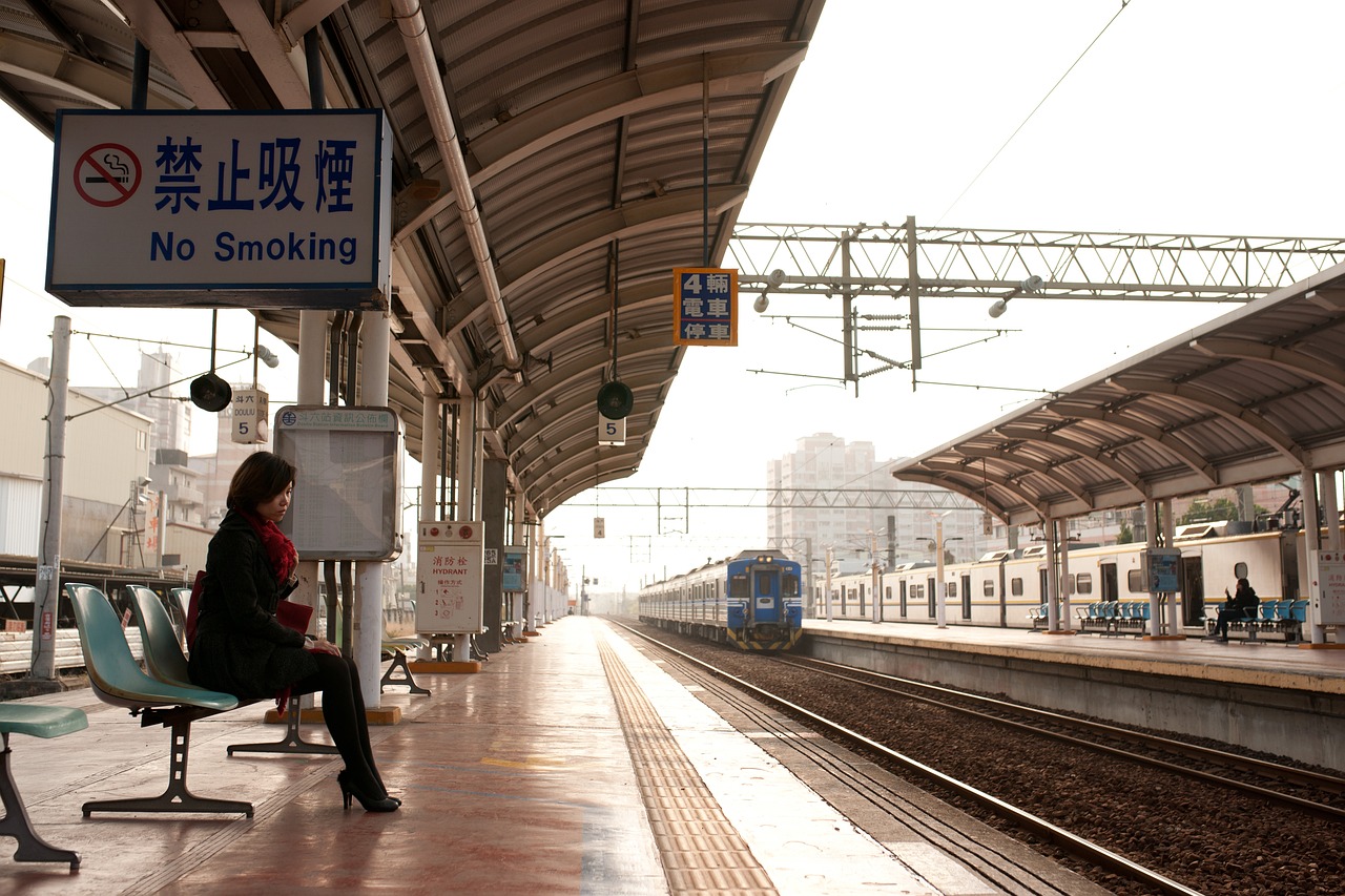 電車のホームでスマートフォンを操作しながら電車を待つ女性