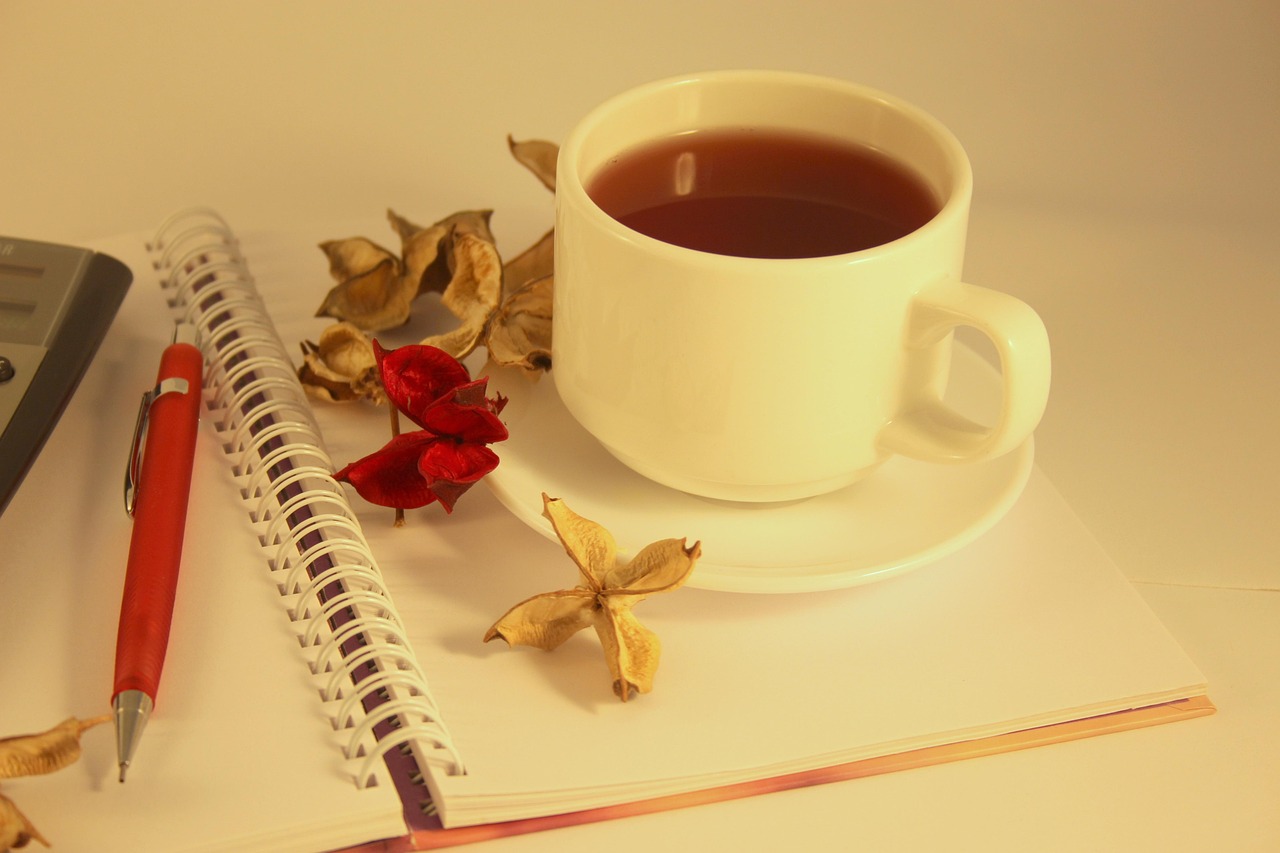 ノートの横に置かれた湯気の立つ紅茶(温かい飲み物)
