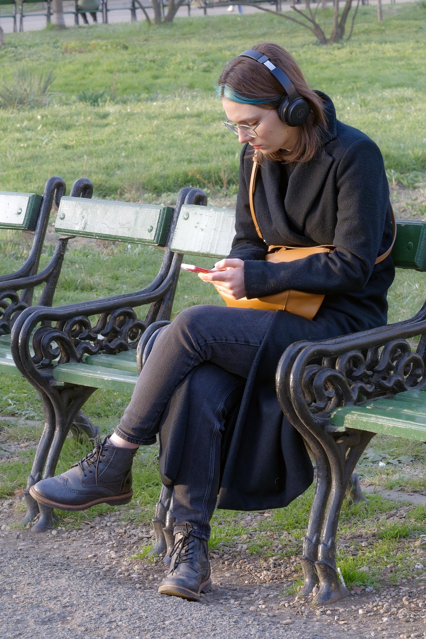 公園のベンチでヘッドホンをつけてスマートフォンを操作する女性