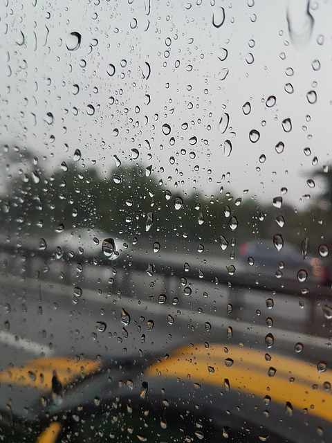 雨粒がついた車の窓ガラス越しに見える道路の風景、車の水没被害をイメージ