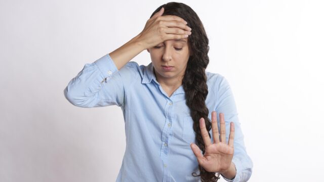 額に手を当ててうんざりした表情を浮かべる女性、お盆明けのだるさや疲れを表すイメージ