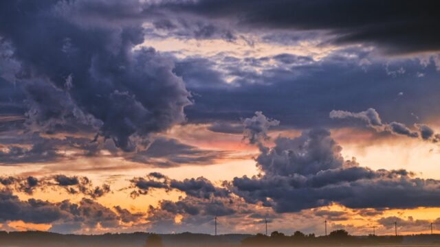 暗い積乱雲が広がる夕暮れの空と、遠くに見える風車のシルエット。台風・低気圧接近のイメージ