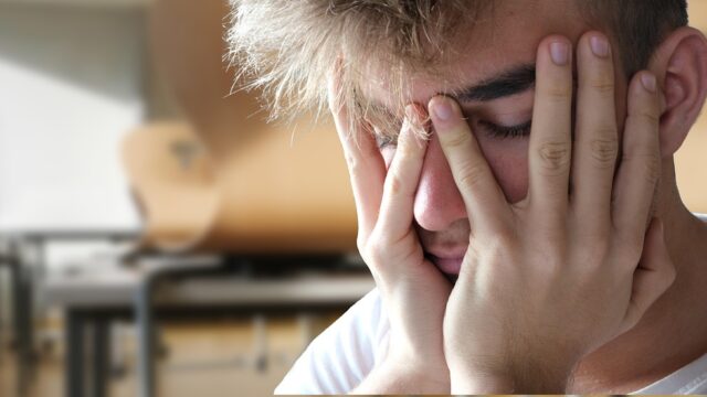 両手で顔を覆い、思い詰めた表情を浮かべる男性の写真