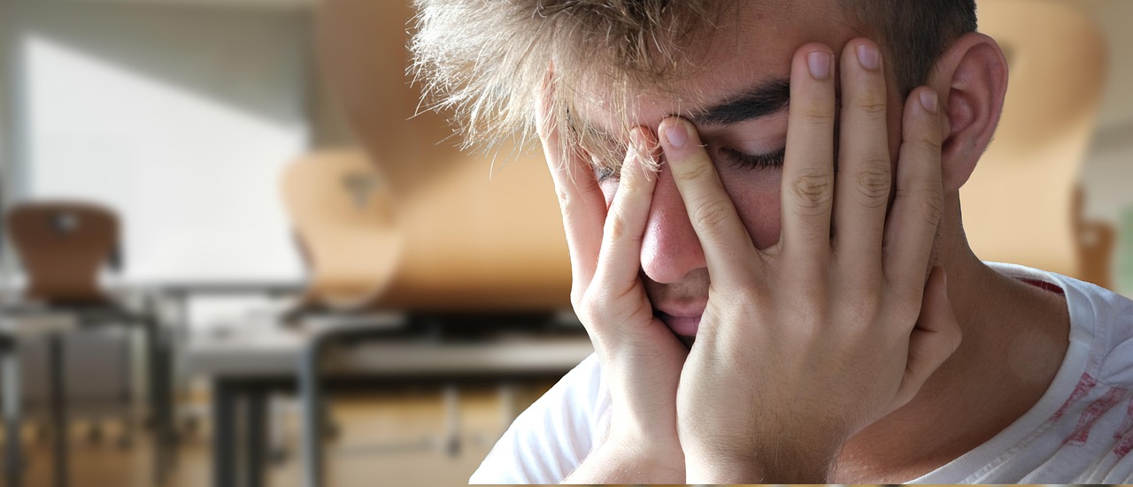 両手で顔を覆い、思い詰めた表情を浮かべる男性の写真