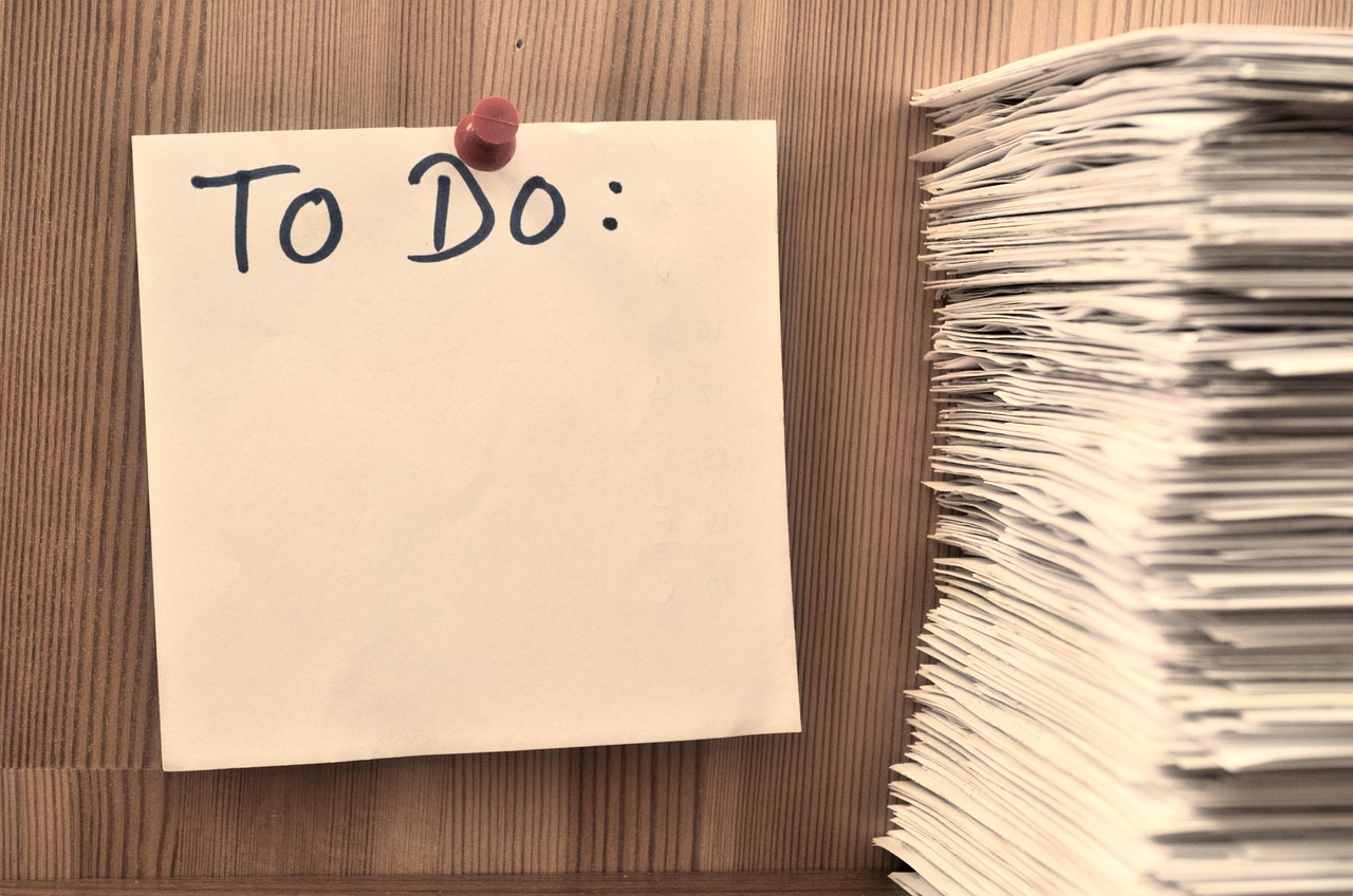 壁に貼られた「TO DO」の付箋と積み重なった書類の束