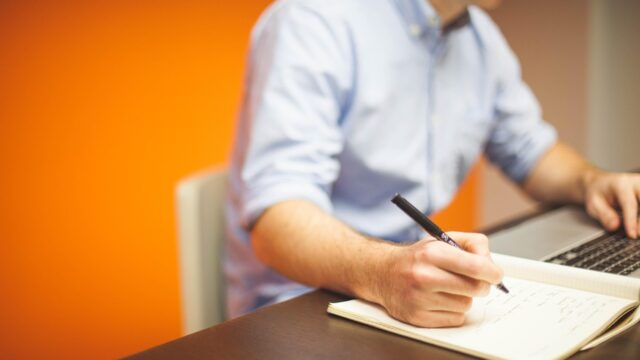 ノートパソコンの前でメモを取りながら仕事をする会社員の手元