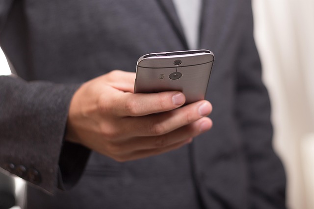 スーツ姿の人がスマートフォンを片手で操作している手元