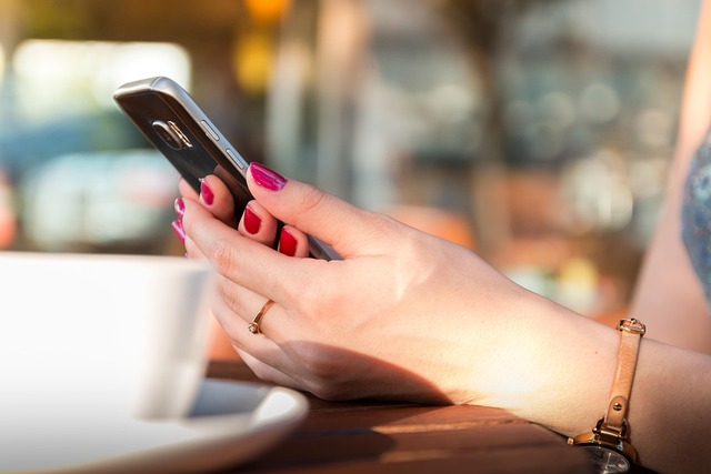 カフェでコーヒーを片手にスマートフォンを操作する手元のクローズアップ
