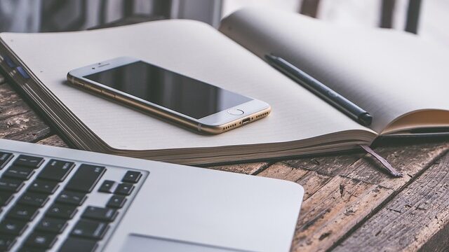 机の上に置かれたノートパソコンとスマートフォン、開いたノート