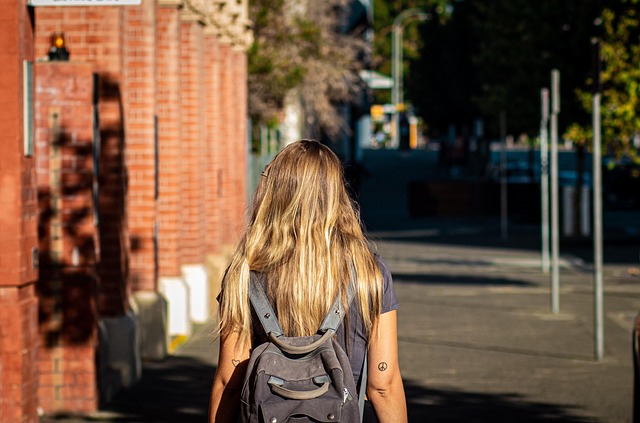 リュックを背負い、日差しの差し込む道を歩く女性の後ろ姿