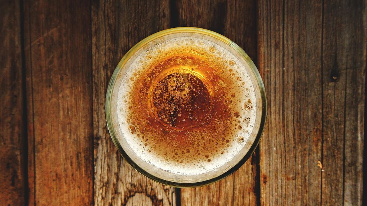 木のテーブルに置かれたビールのグラスを真上から写した写真