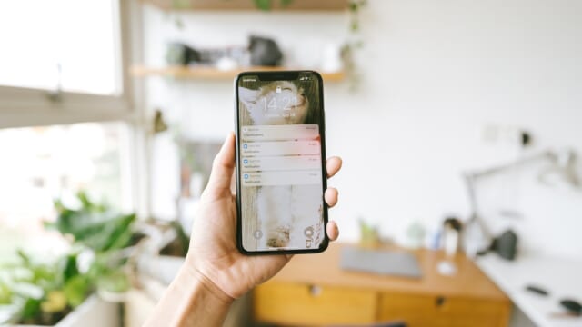通知が並ぶロック画面のスマートフォンを手に持っている様子