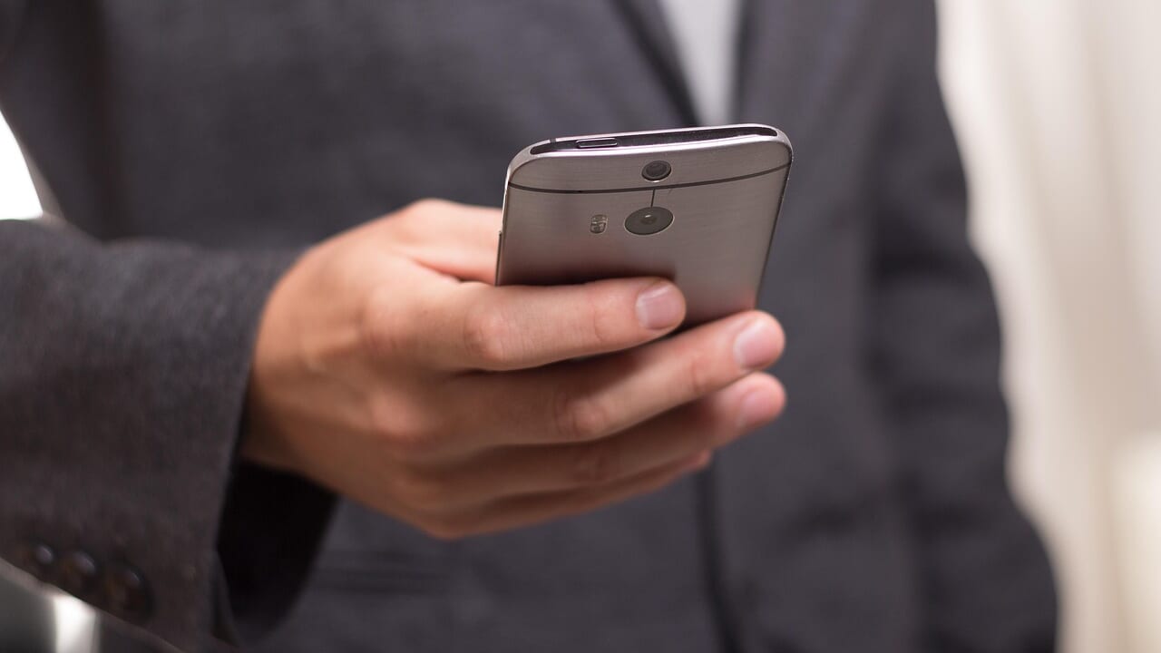 スーツ姿の人が片手でスマートフォンを操作している手元