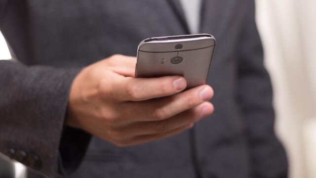 スーツ姿の人が片手でスマートフォンを操作している手元