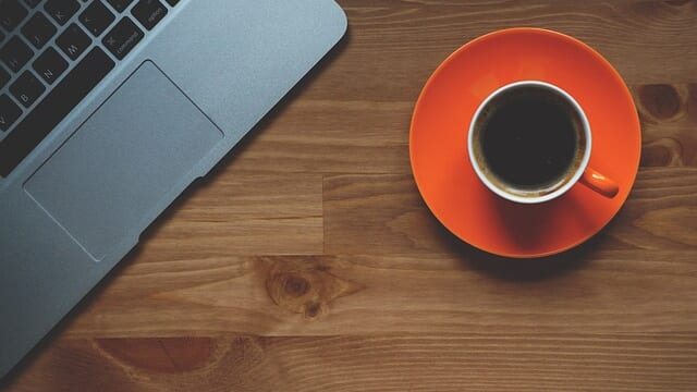 机の上のノートパソコンとオレンジ色のコーヒーカップ