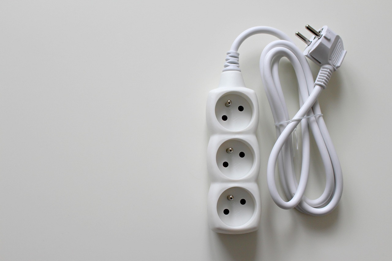 白い台の上に置かれた、3つ口の白い電源タップと電源プラグ