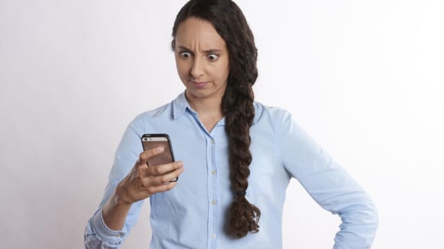 スマートフォンの画面を見て、驚いたように眉を寄せる女性