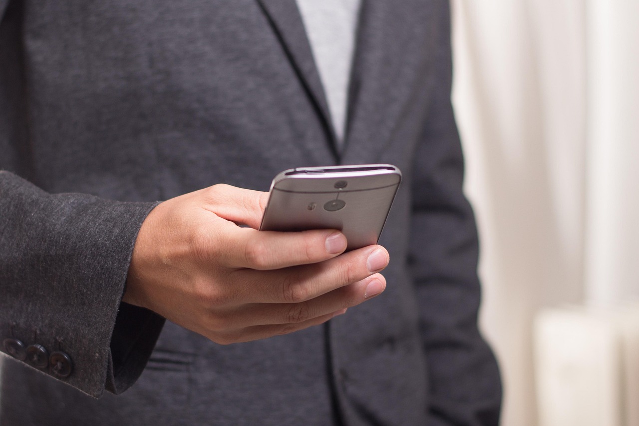 スーツ姿の人が片手でスマートフォンを操作している様子