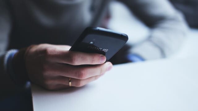 テーブルの上でスマートフォンを片手で持つ手元