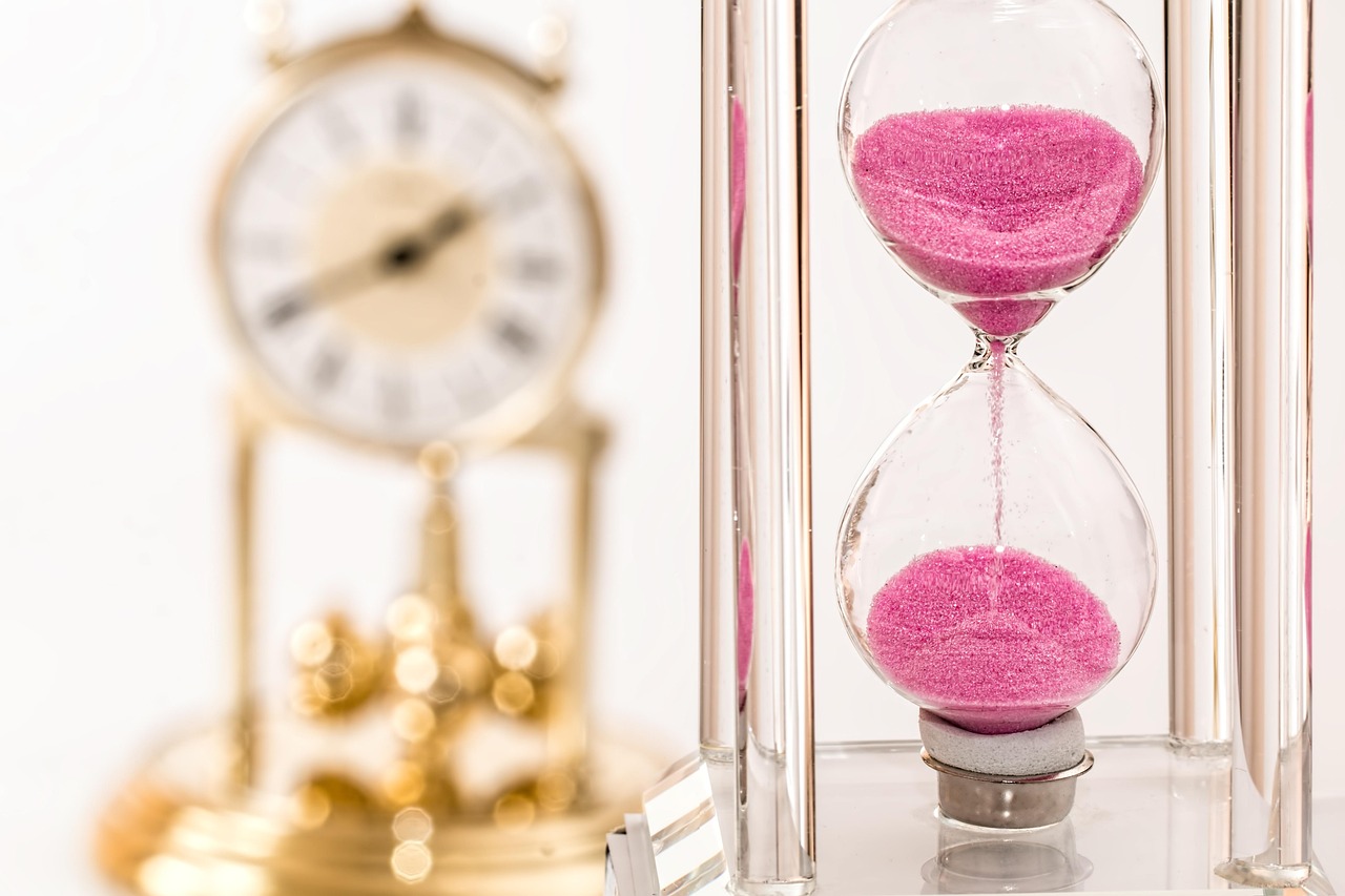 ピンク色の砂が落ちる砂時計と、奥にぼやけた置き時計
