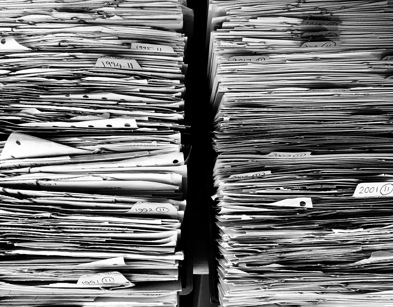 紙の書類が棚に高く積み重なっている白黒の写真