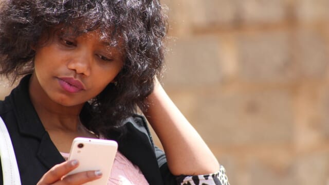 スマートフォンの画面を見ながら髪に手をやり、首をかしげる女性