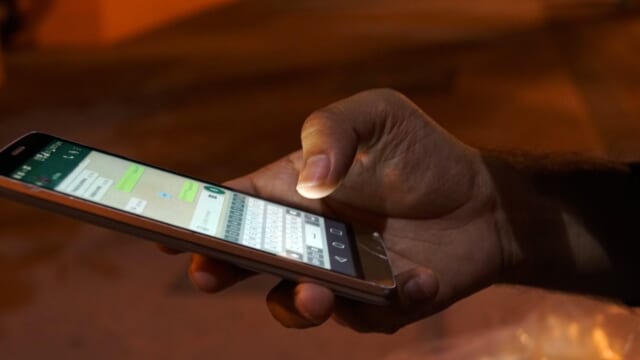 チャットアプリの画面を開いたスマートフォンを片手で操作する手元