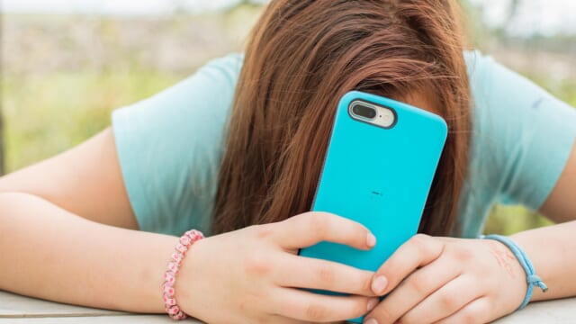 テーブルに突っ伏して、水色のスマートフォンを顔の前に持つ人