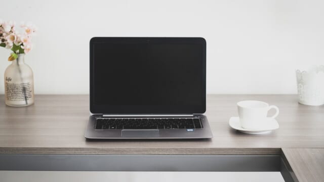 木目のテーブルに置かれたノートパソコンとコーヒーカップ