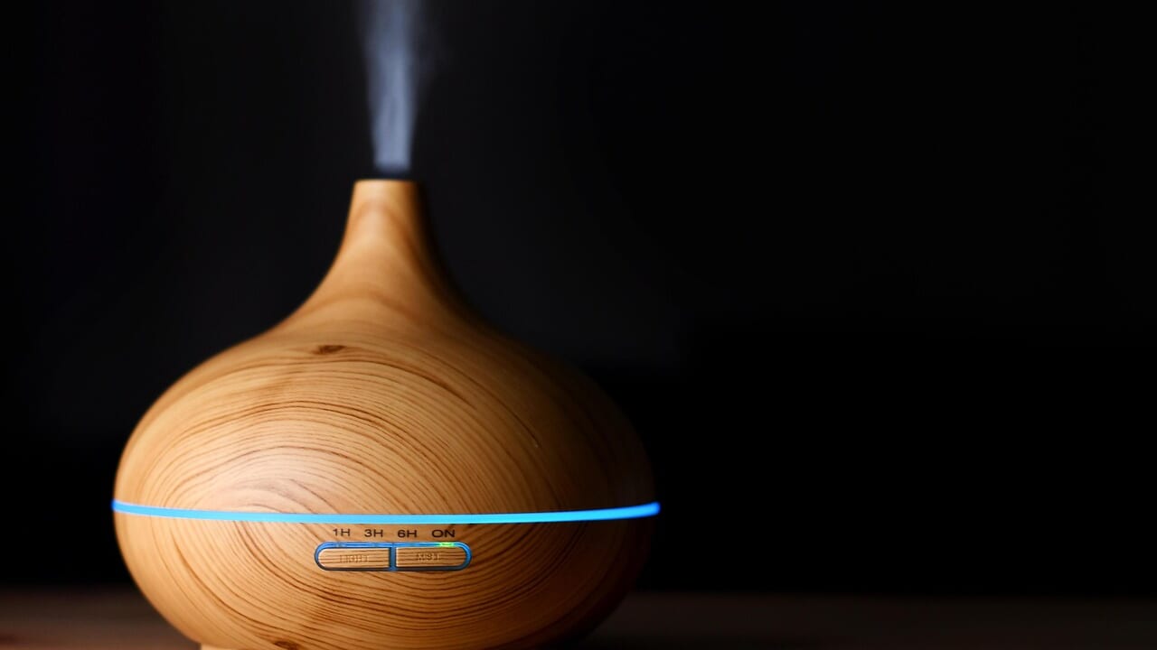 暗い部屋で白い蒸気を出している木目調の卓上加湿器