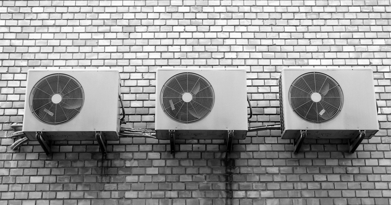 れんがの壁に並んで取り付けられた、エアコンの室外機3台(白黒写真)