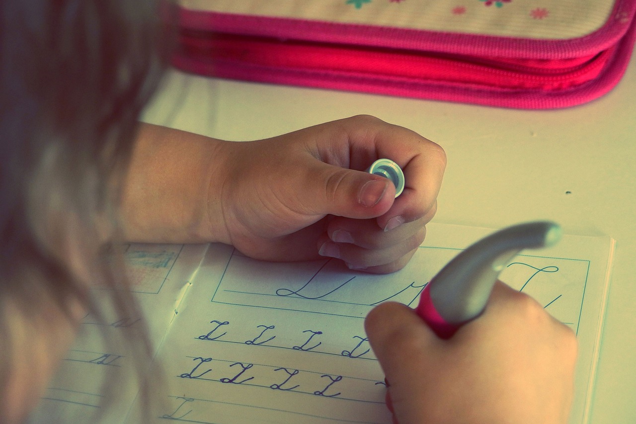 ペンケースの前でノートに文字の練習をする子どもの手元