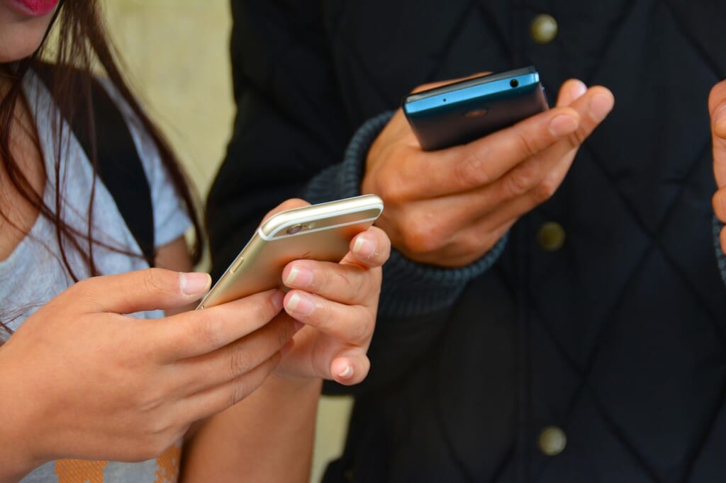 並んでそれぞれスマートフォンを操作している2人の手元