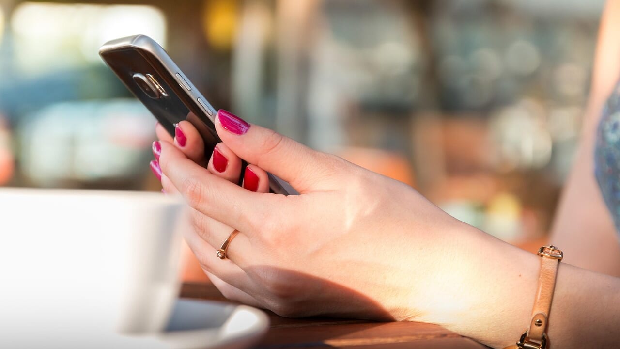 カフェのテーブルでスマートフォンを手に持っている女性の手元