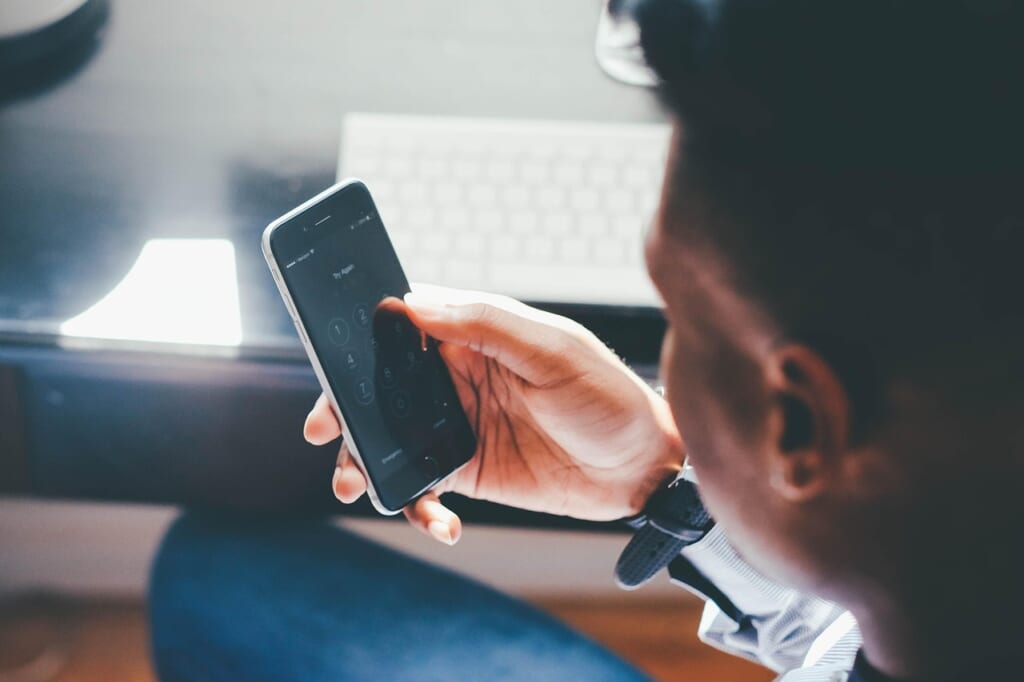 パスコードの入力画面が表示されたスマートフォンを持つ男性