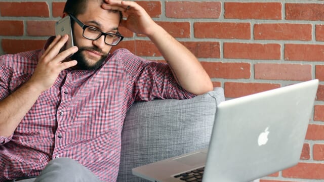 ノートパソコンを前に、電話をしながら額に手を当てて困った表情の男性