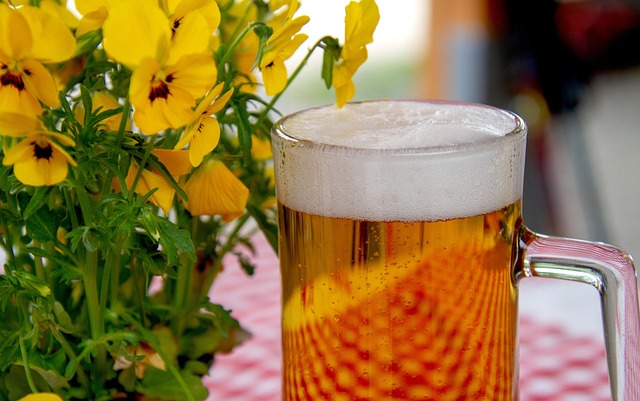 黄色い花のそばに置かれたビールジョッキの写真、ビール系飲料の税金をイメージ