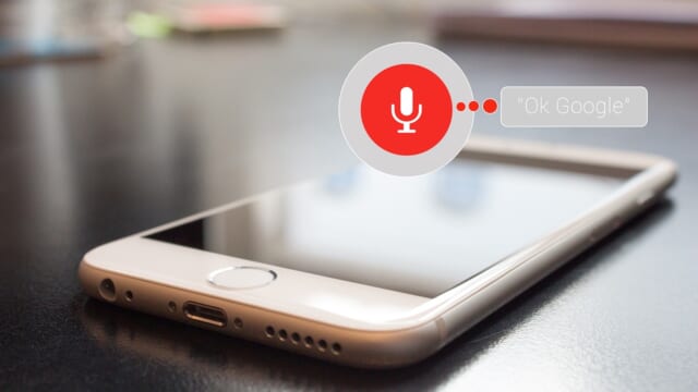 テーブルに置かれたスマートフォンと「Ok Google」のマイクのアイコン