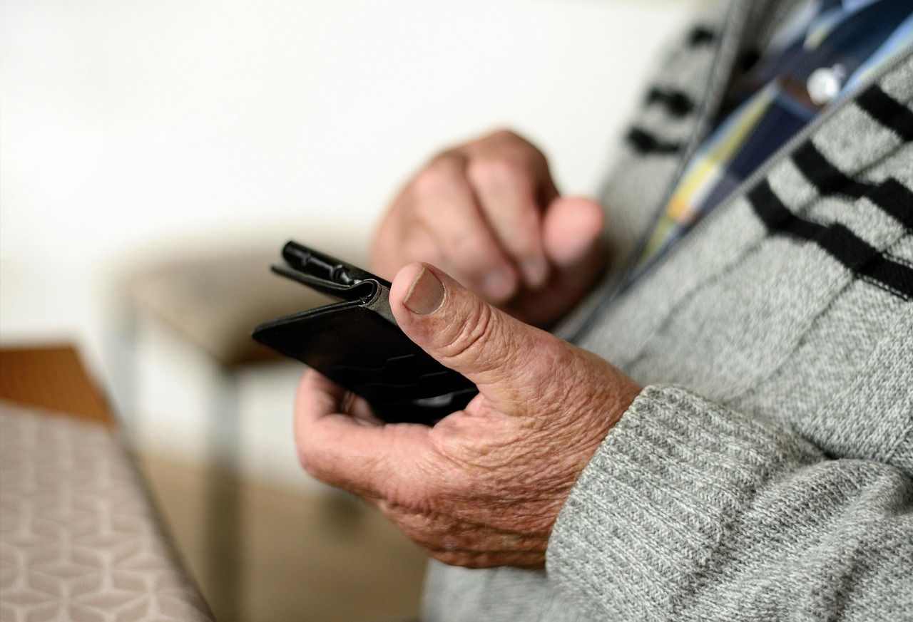 手帳型ケースのスマートフォンを手に持つ年配の人の手元