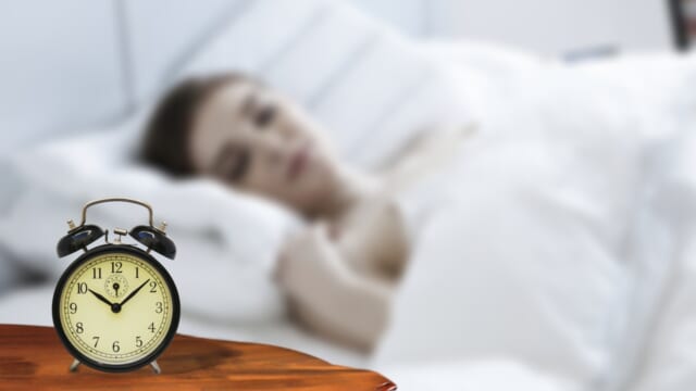 ベッドで眠る女性と、手前の台に置かれた目覚まし時計