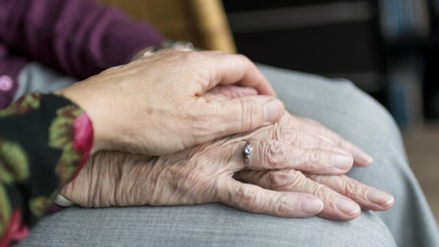 高齢の人の手に、家族がそっと手を重ねている様子