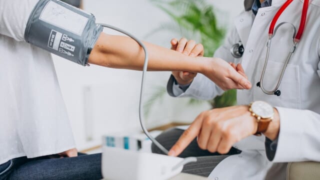 医師が患者の腕に血圧計のカフを巻いて血圧を測っている様子